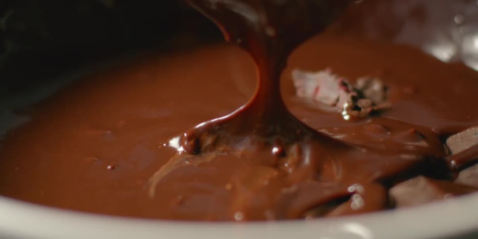 A piece of dessert is dipped into melted chocolate
