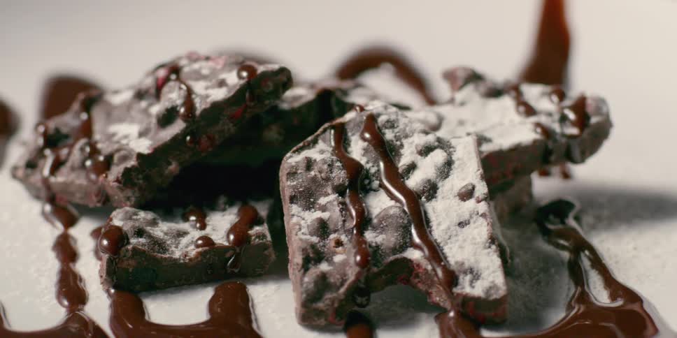 Brownies are on a plate drizzled with chocolate sauce and powdered sugar