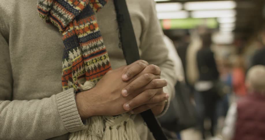 A woman is standing with her hands together on a subway platform