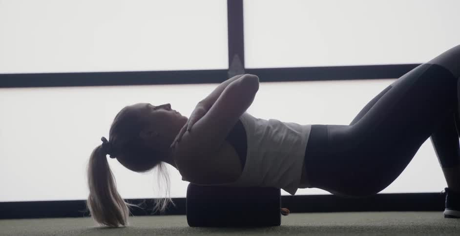 A woman is laying on a rolling pad and stretching her back