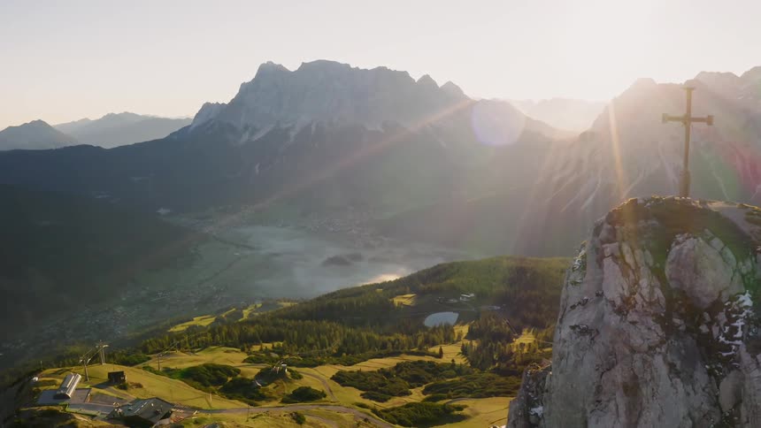 Mountain peak where a cross has been raised overlooks green valley