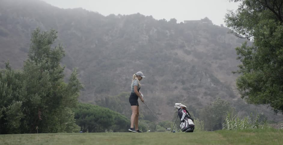 A woman places a golf ball on the tee and takes a practice swing