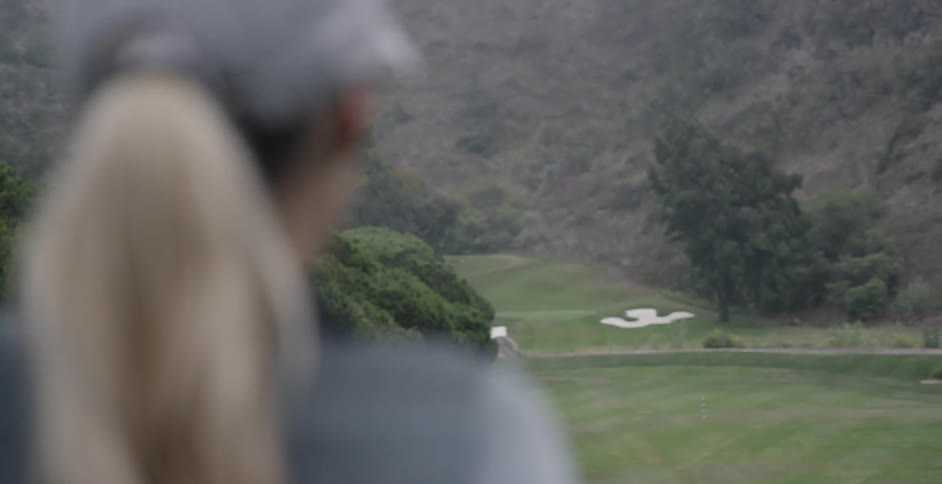 A female golfer is looking down a fairway during the day