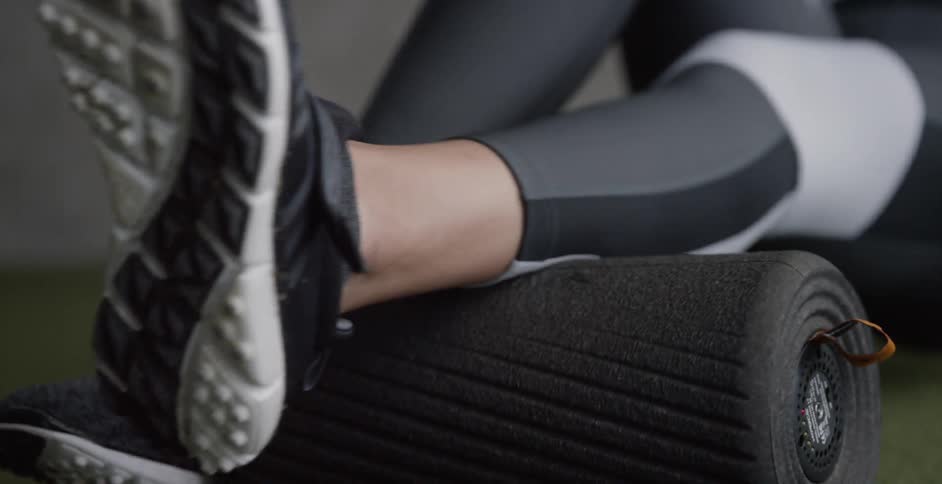 A woman uses a roller to massage her calf muscle at the gym