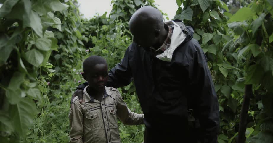 A man and a child are standing in a forest and the man pats the child on the back