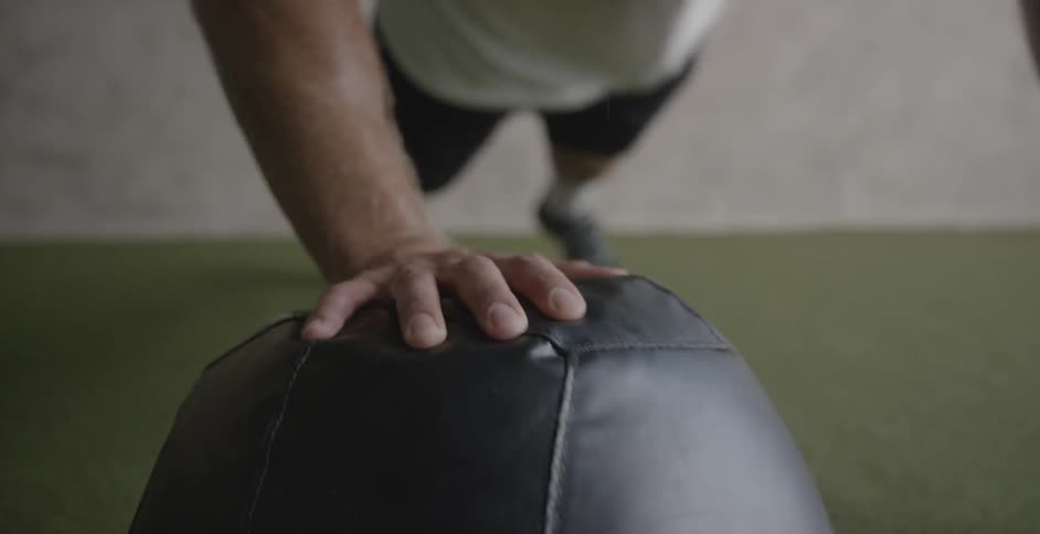 A man is working out using a medicine ball inside a gym during the day