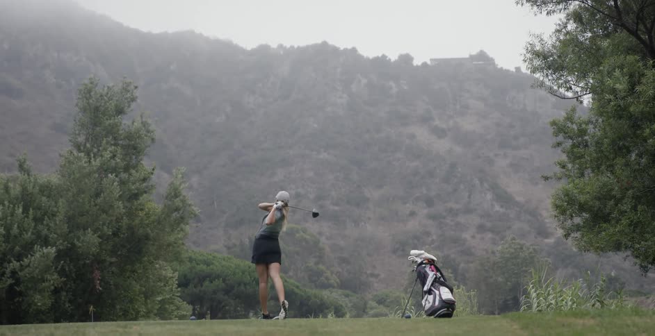 A female golfer is driving the ball down the fairway on a course during the day