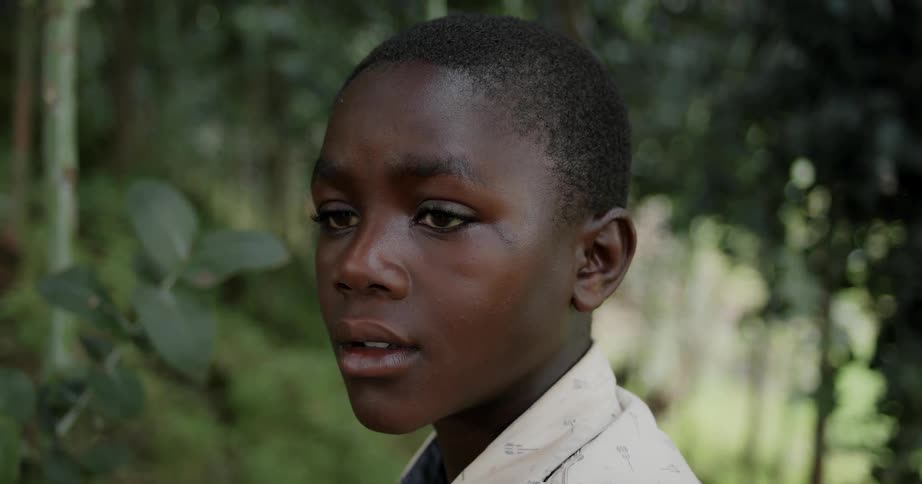 A young boy is standing still and looking around in a jungle