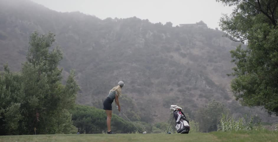 A woman walks up to the ball on the tee and prepares to drive