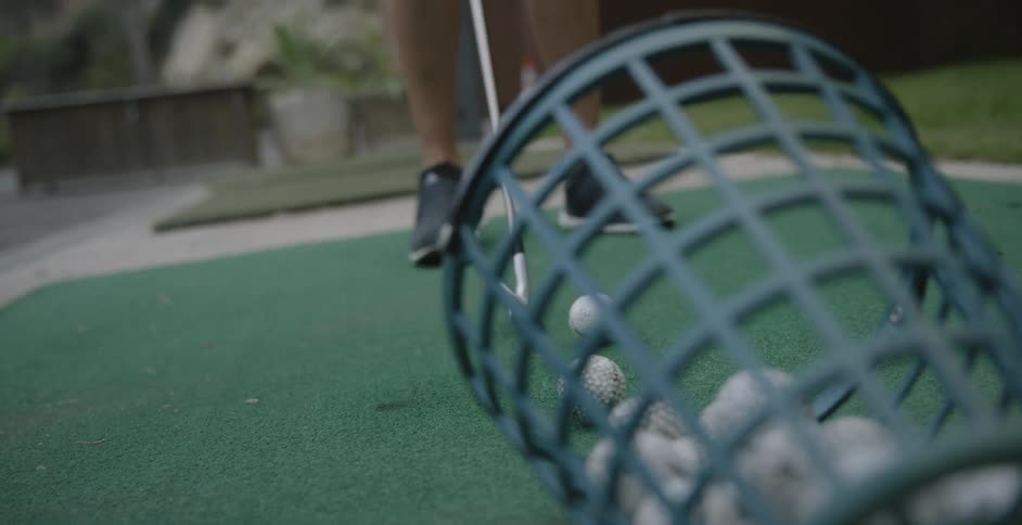 A woman selects a golf ball and sets at the driving range