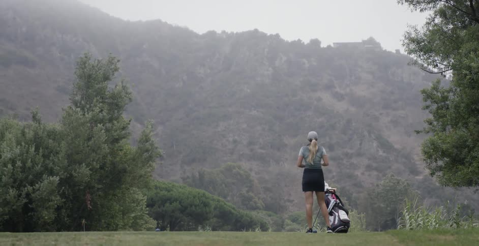 A woman sets down her golf bag on the green