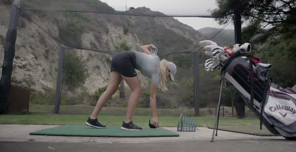 A woman places are golf ball on a tee and prepares to hit it with her golf club