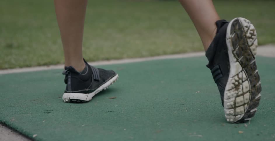 A female golfer twists her foot as she drives the ball at a driving range