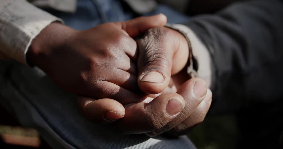 A man is clasping a boy's hand in his outside during the day