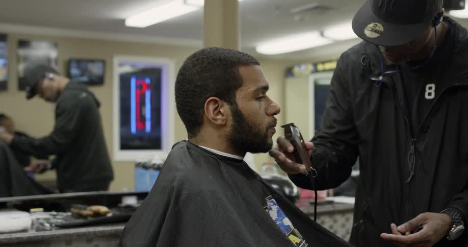 A barber trims a man's mustache and beard with clippers