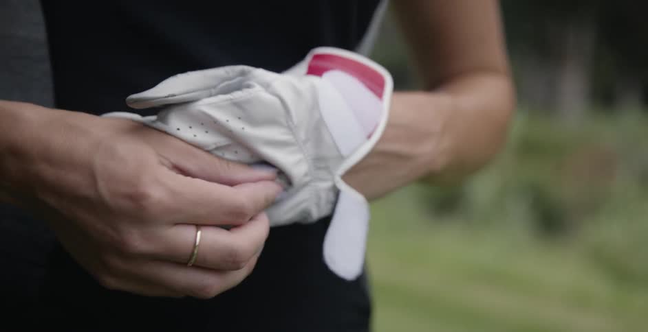 A woman takes off a glove on a golf course