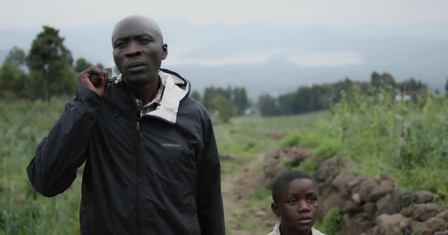 A man and a young boy are standing in a field the man has a large knife