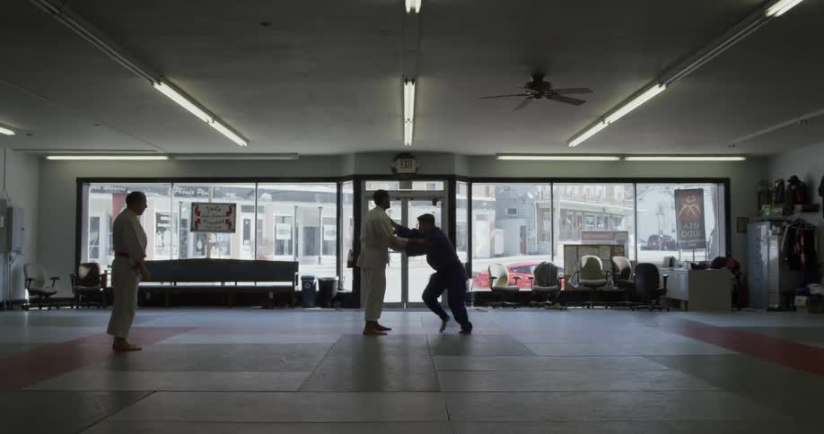 Two men are practicing martial arts moves as an instructor looks on inside a dojo during the day