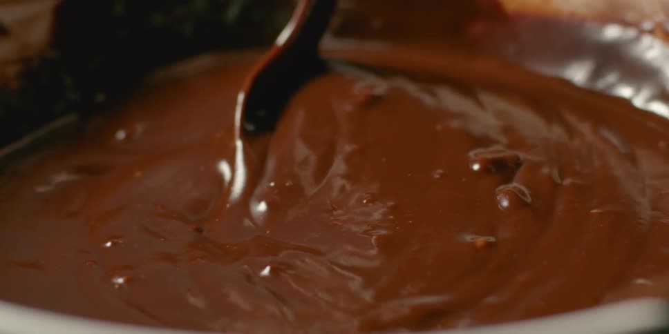 A bowl of melted chocolate is being mixed with a spoon