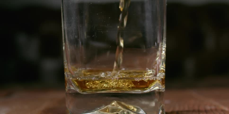 A gold colored liquor is poured into a glass