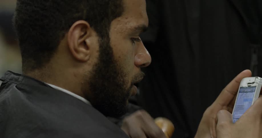 Man looks at phone while sitting in barbershop chair