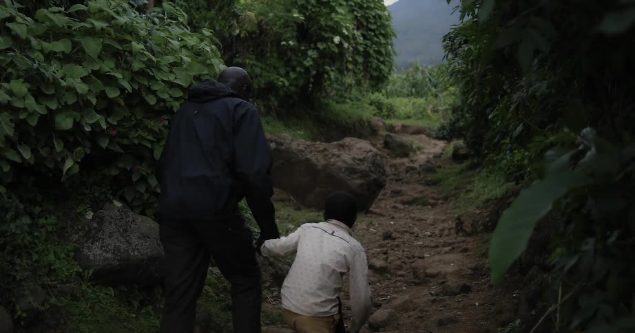 A man and boy hold hands on a dirt path