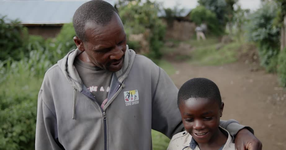 Man with his arm around a boy as they walk along a dirt path