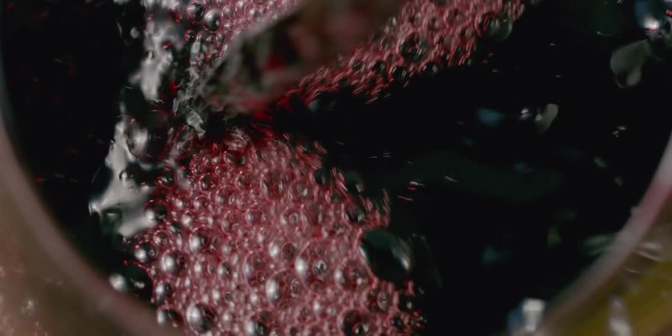 Red fluid bubbles as it is poured into a cup