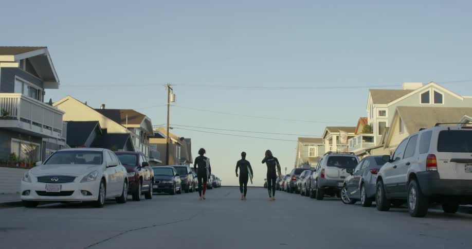 Surfers walk on a street with surfboards