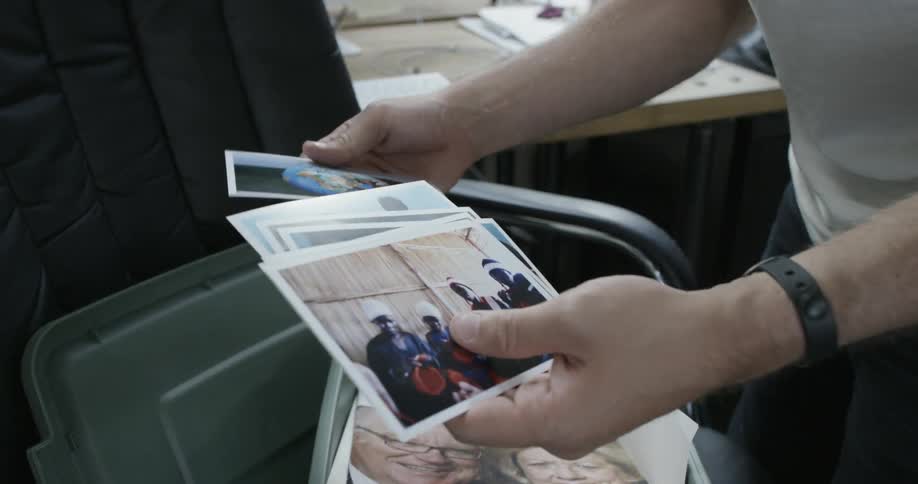 Man sorting through a handful of photographs over a bin