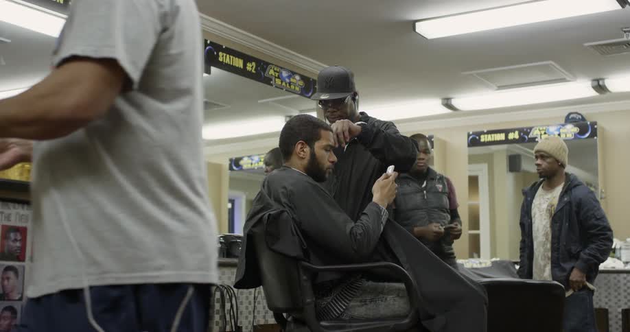 A barber is styling a customer's hair as men mill about in a barbershop