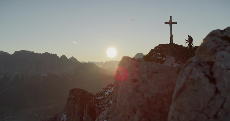 Hikers climb up to a cross on a mountain peak at sunset