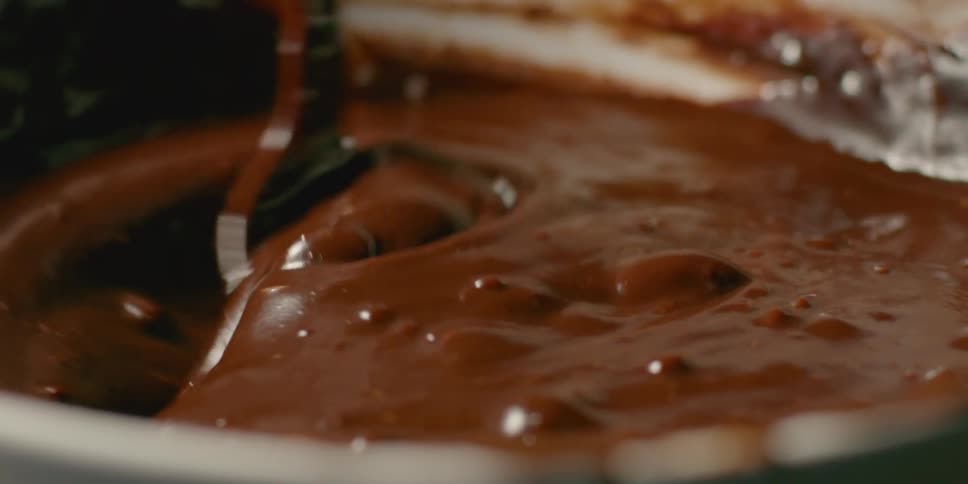 A spoon is stirring chocolate sauce in a pan