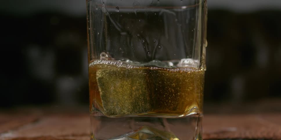 Sugar cubes are dropped into a shot glass causing the liquor to splash out