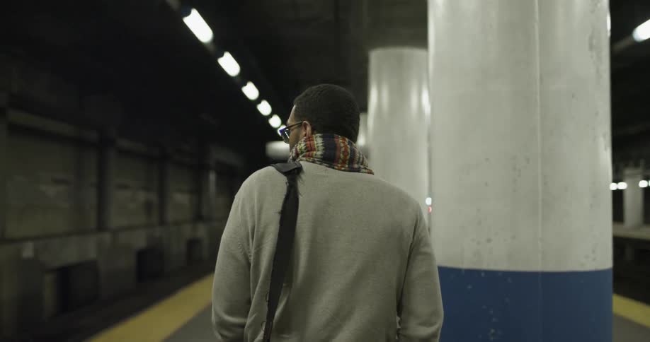 A man wearing a scarf is walking through a subway