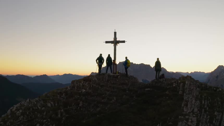 Climbers stand on the peak next to the cross at sunset