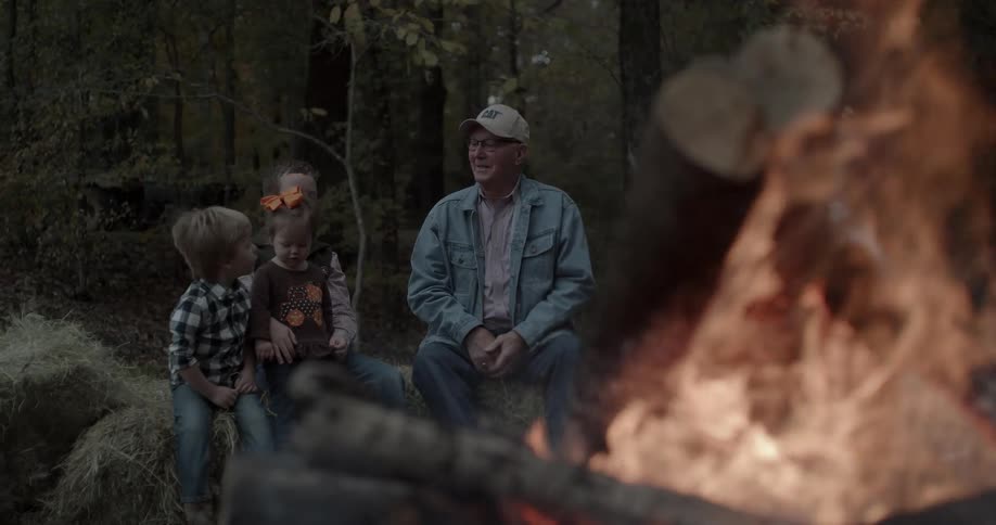 A man and kids sit next to a campfire