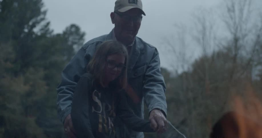 A grandfather and child stir a campfire together