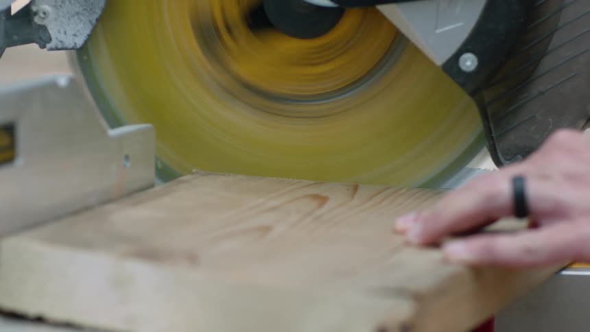 A person lowers the circular saw and cuts through a wooden board