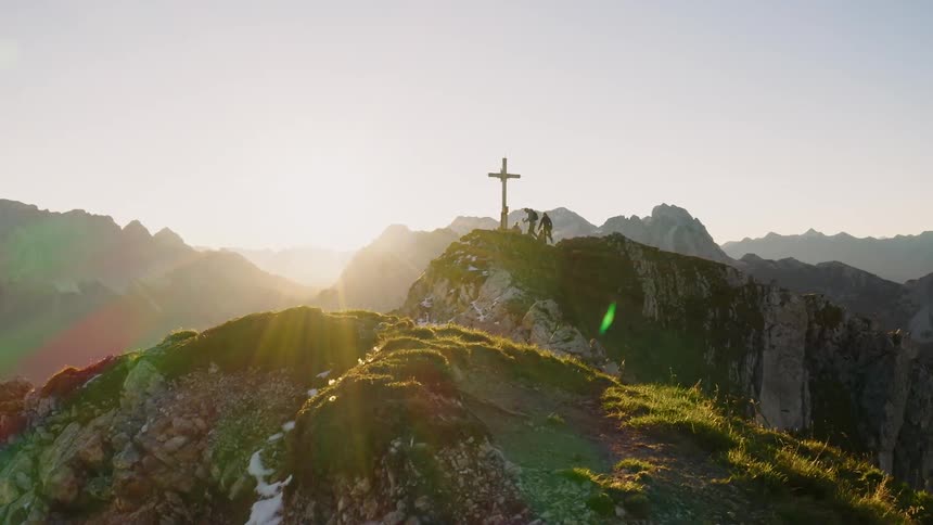 People summit a mountain ridge with a cross on it