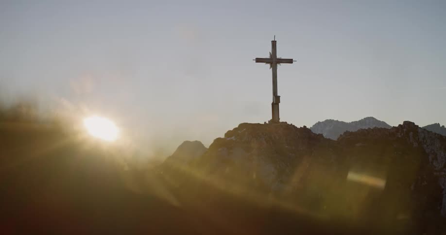 A cross sits on top of a hill with the sun shining on it