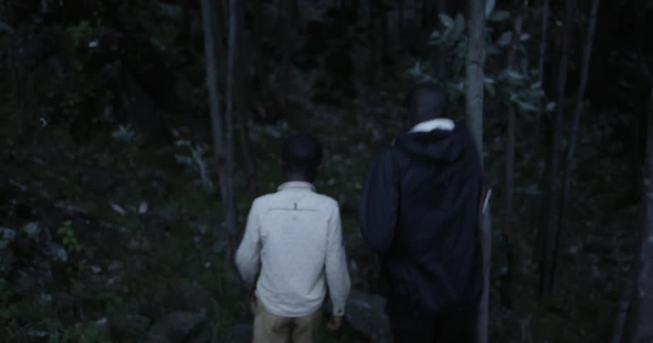 A boy and a man walk through a slightly dark wooded area