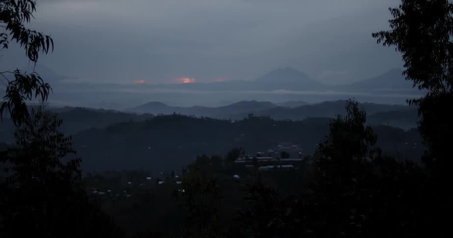 The sun sets on the horizon over trees and hills