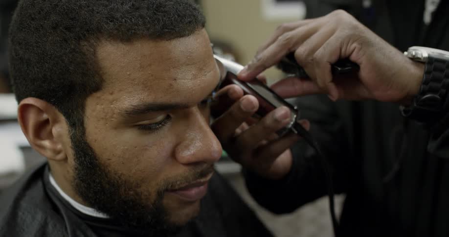 Man shaving another man's head in a barber shop