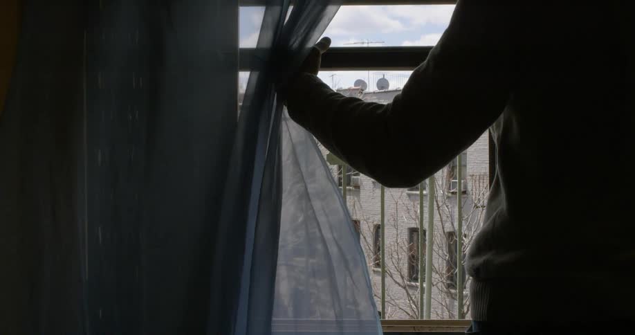 A person opens the blind to look out the window