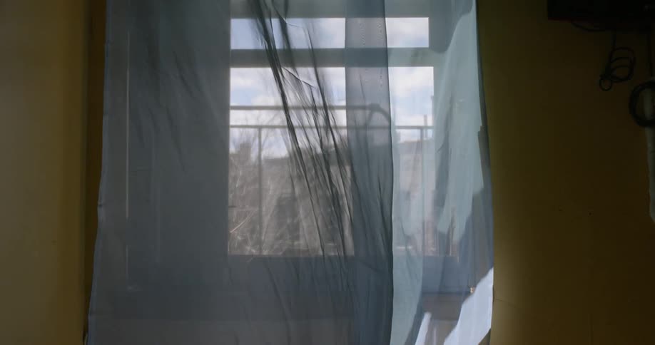 White curtains are blowing in the breeze of an open window