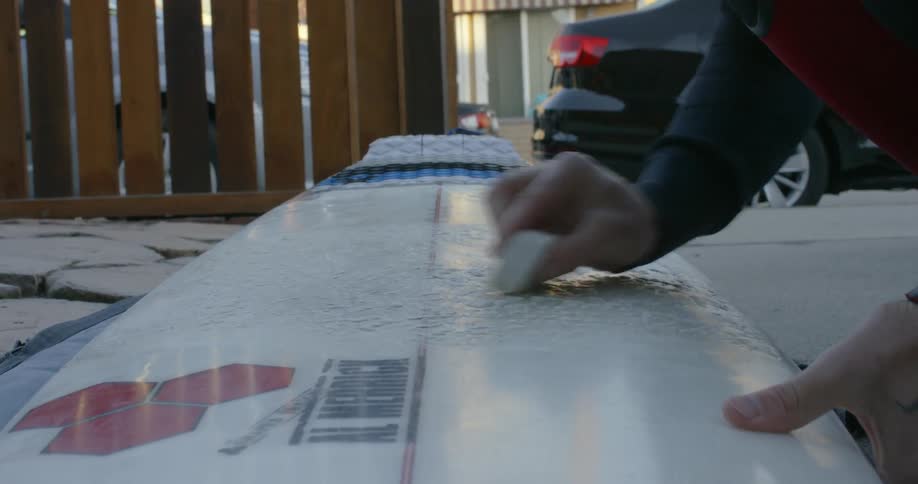 A person waxes a surfboard outside