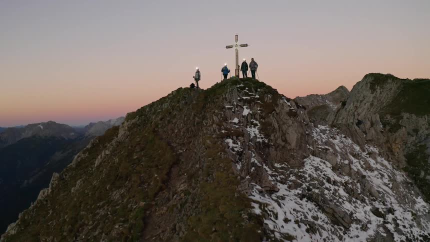 Four people holding hiking sticks stand on top of a mountain near a large cross