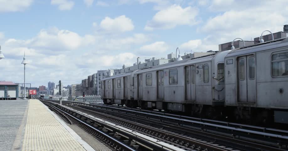 A train slowly goes by a city platform on a sunny day with clouds in the sky