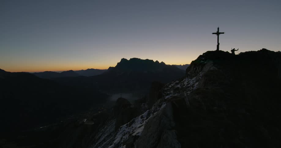 Hikers climb up to a cross on a mountain peak at dusk